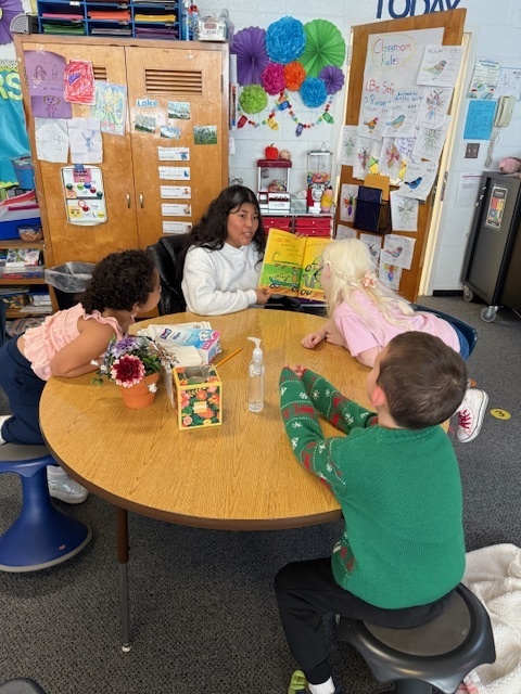 Middle school student reading to three first grade students. 