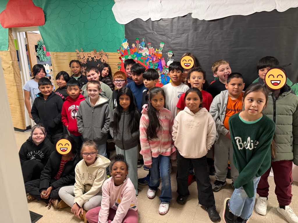 4th grade students stand in front of their Santa's sleigh door and hall decorations smiling. 