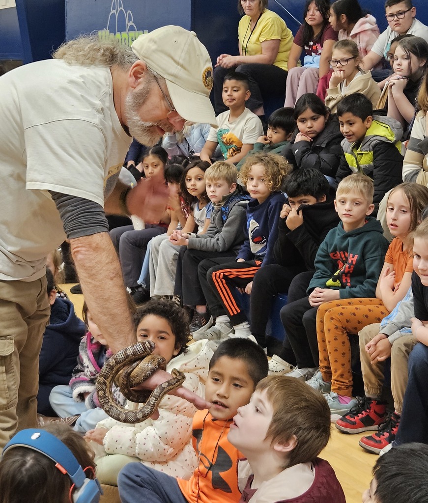 Man holding snake up to 3 students with large crowd of students behind them. 