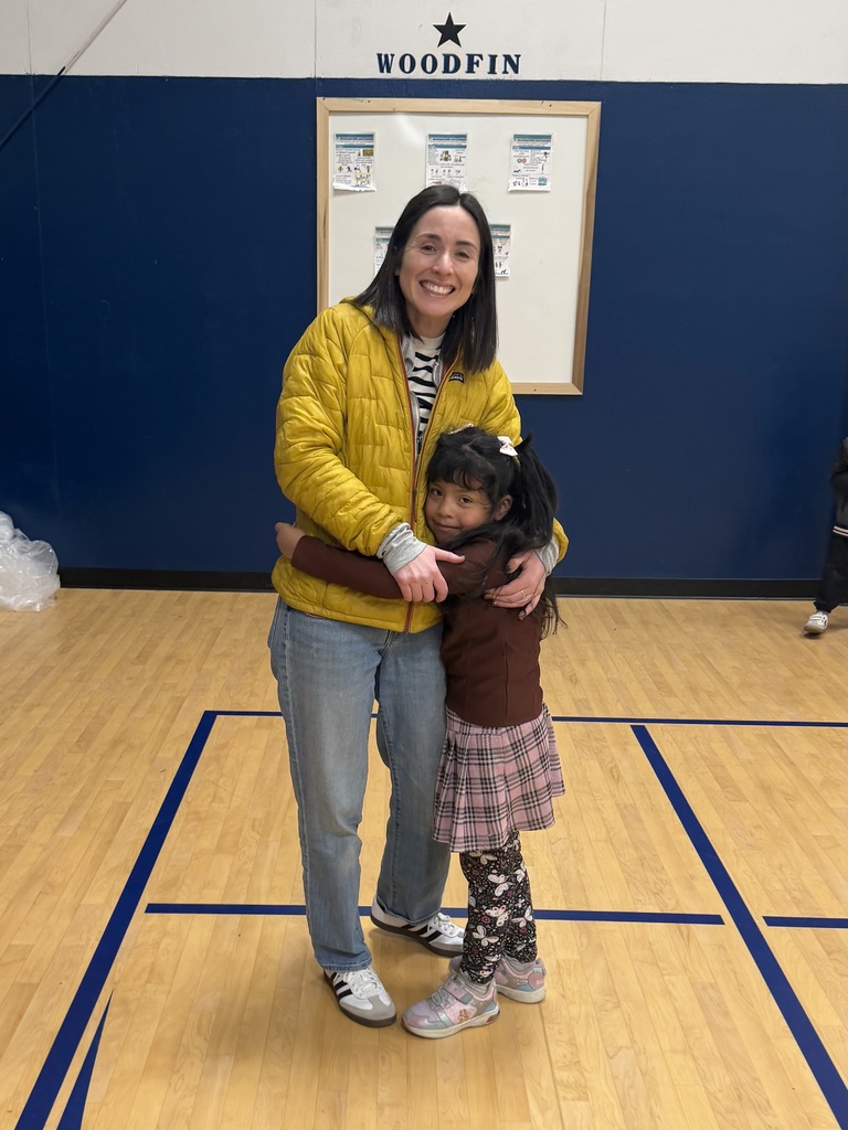Teacher and student embrace while smiling for photo.