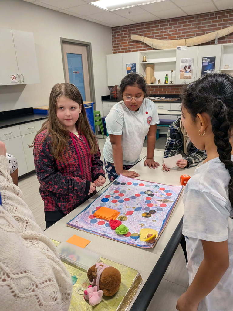 Students stand around game table with their board game.