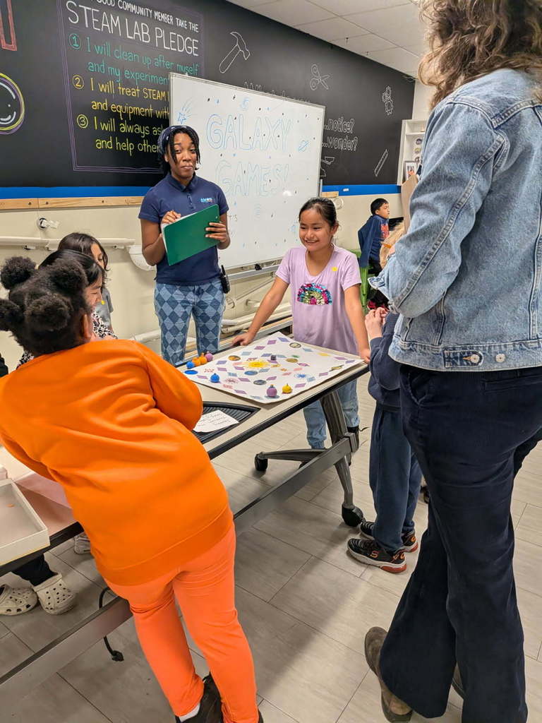 Students stand around game table with their board game.