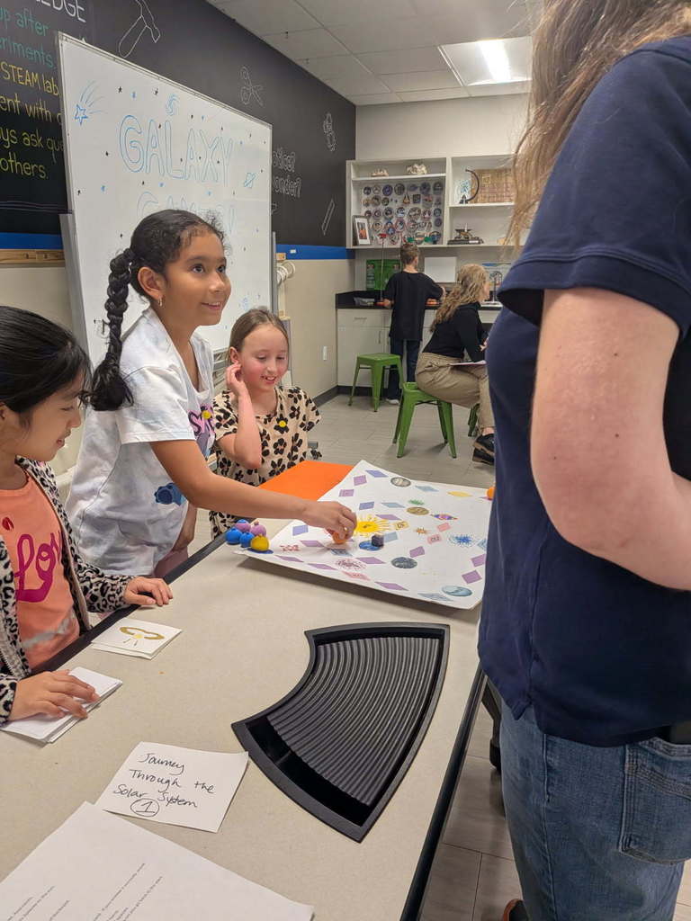 Students stand around game table with their board game.