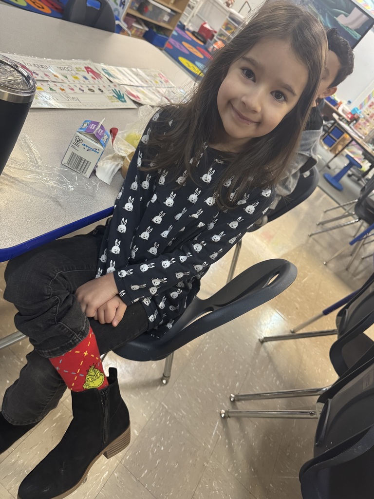Student sitting, smiling, pointing to Grinch sock. 