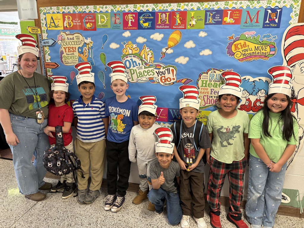 Teacher and students stand in front of Dr. Seuss themed board in paper Cat in the Hat hats. 