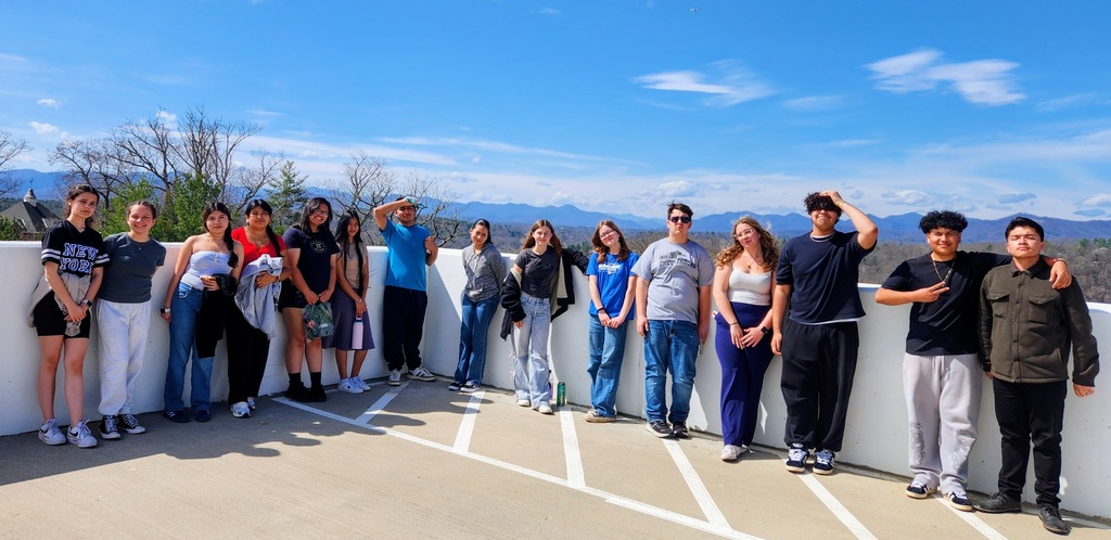 a group of students stands in a parking deck roof with views of mountains behind them
