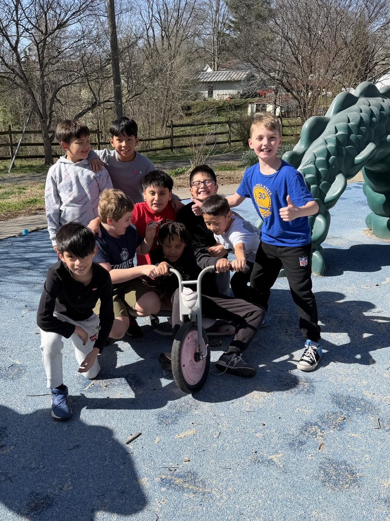 Students stand in group surrounding one student sitting on a tricycle.
