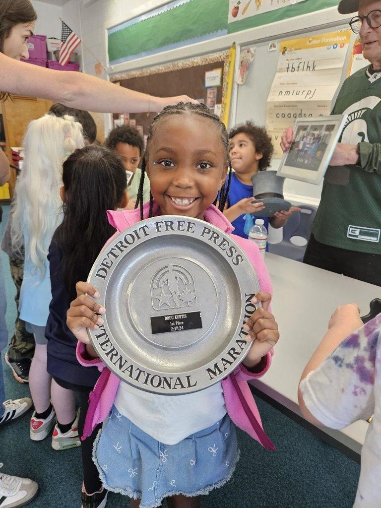 Student stands smiling while holding up a marathon award. 