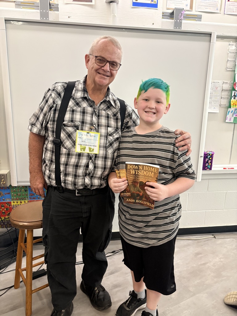 Author and student stand together smiling. Student is holding up his new copy of the author's book. 