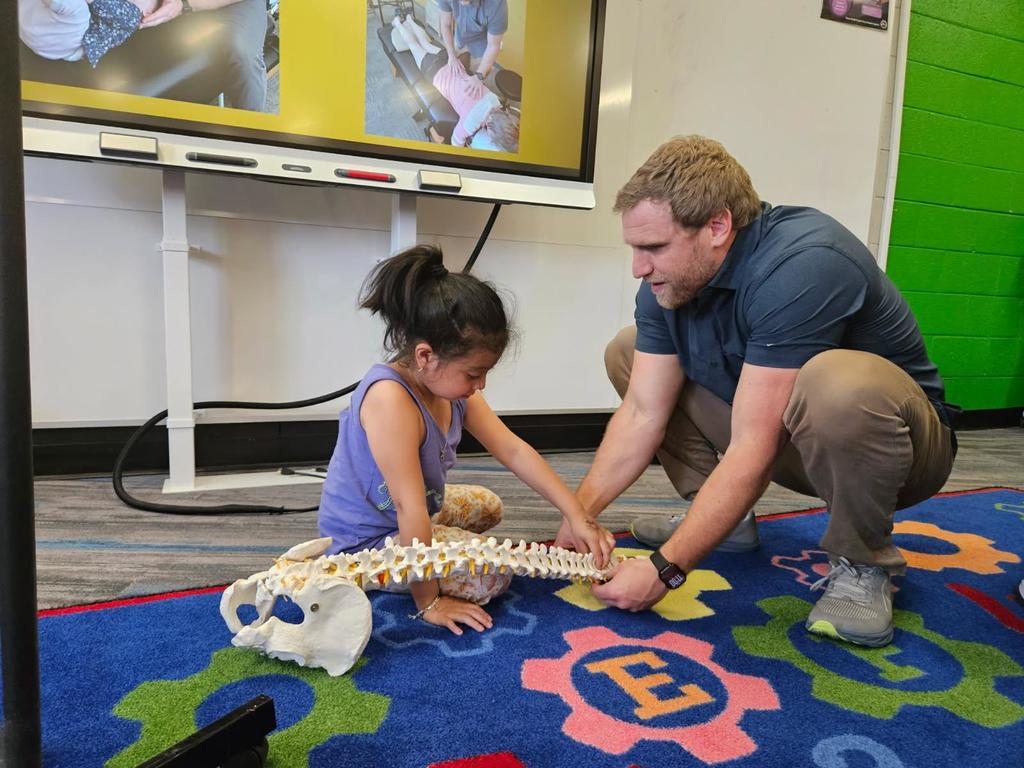 Chiropractor and student squat over a skeleton model of the spine and examine it together. 