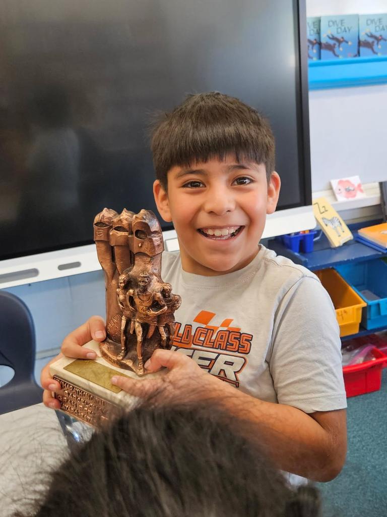 Student stands, smiling, holding marathon trophy. 