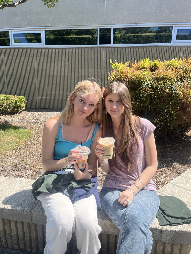 two students sitting on a wall drinking coffee