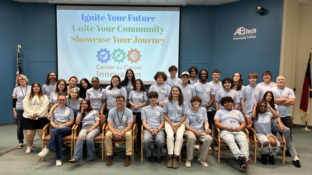 group of students sitting in chairs and standing in rows in front of a projector screen that says Ignite Your Future, Unite Your Community, Showcase Your Journey 