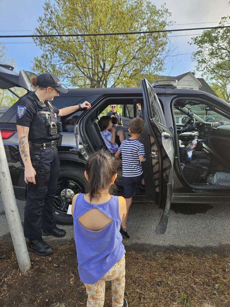 Officer helps students explore police vehicle. 