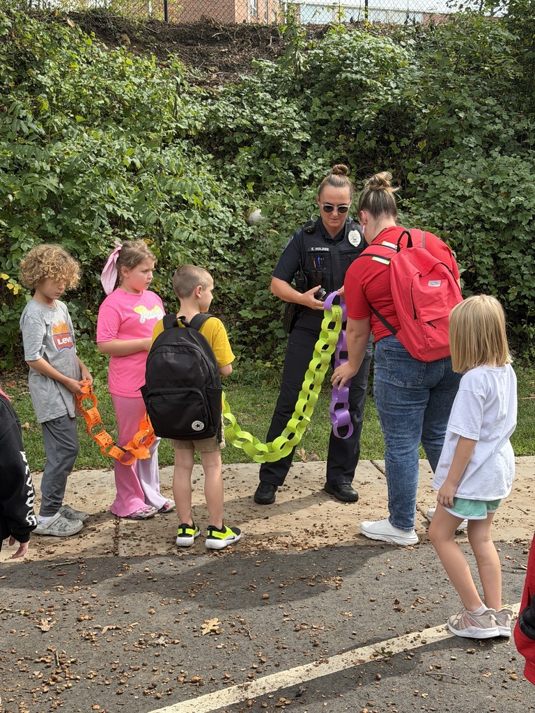 Officer and teacher help connect paper chain as students look on. 