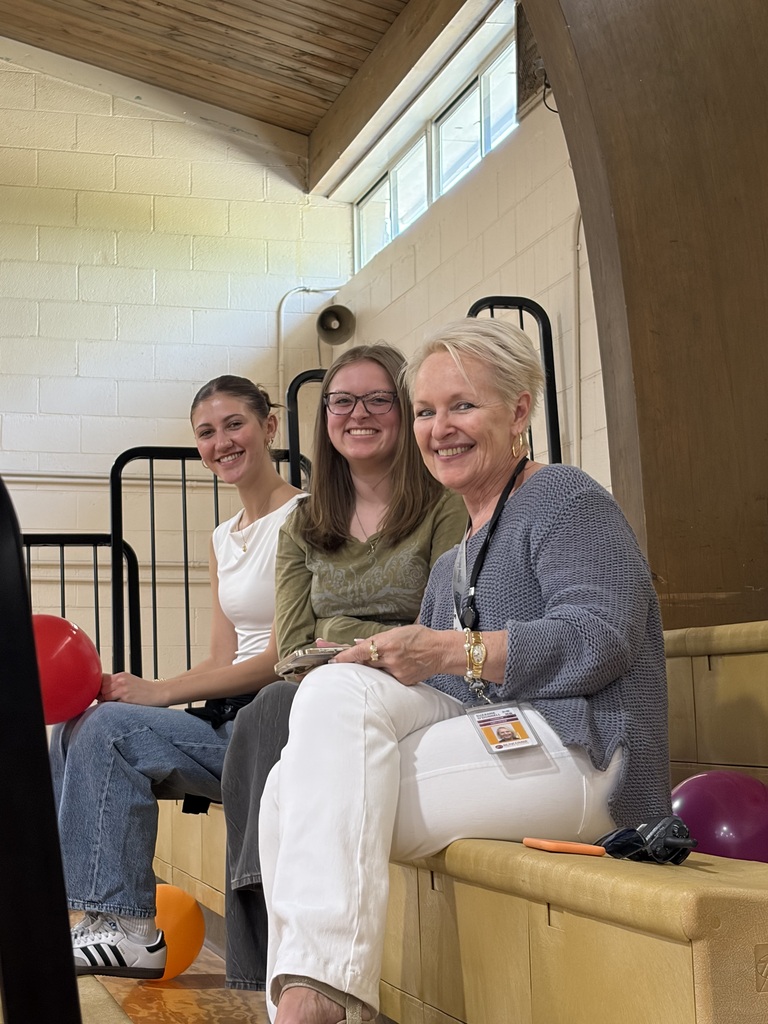 two students and a staff member sitting on gym bleachers 