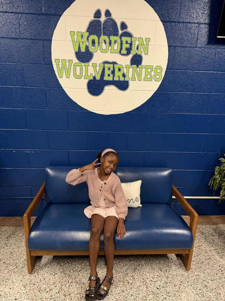 Student in front of Woodfin Wolverine sign sits smiling.