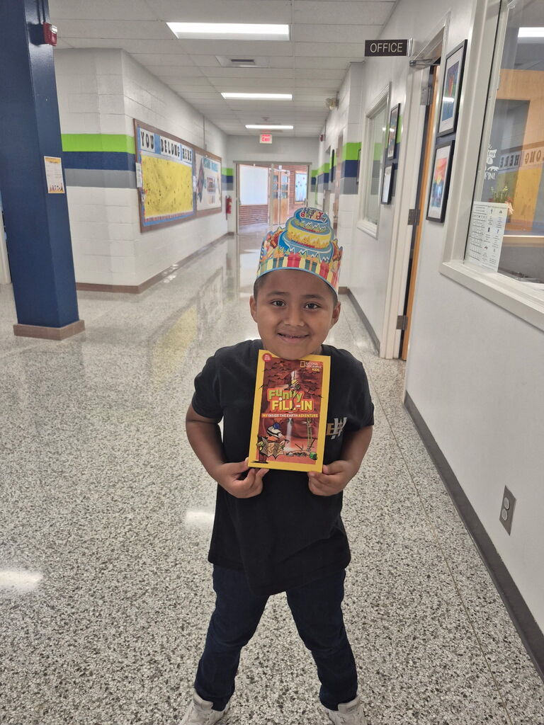 Student stands, smiling, holding book.