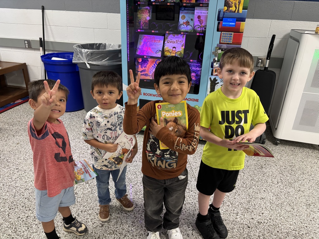 Four students stand in front of book vending machine holding books.