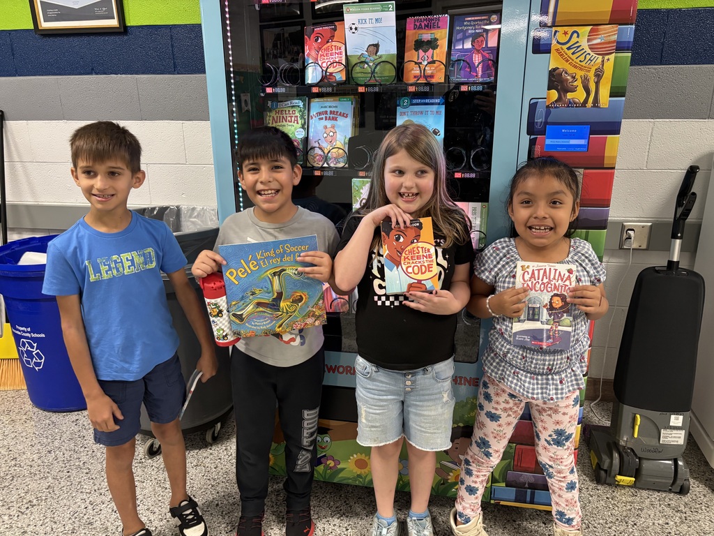 Four students stand in front of book vending machine holding books.