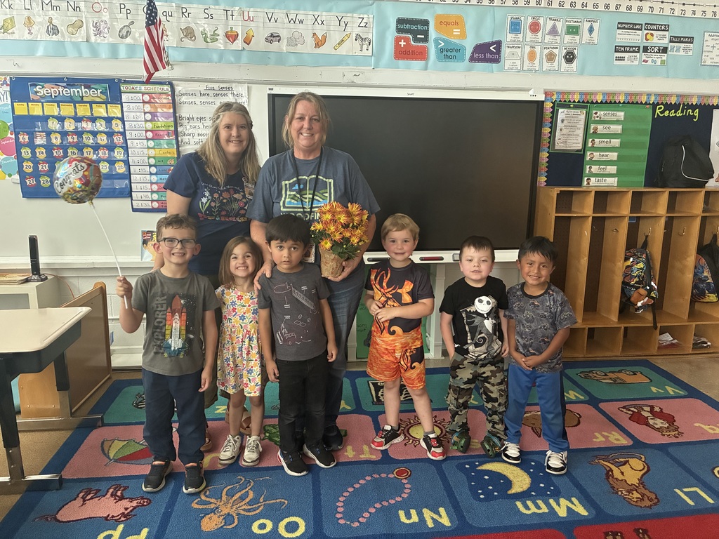 Teacher of the Year, Mrs. Rogers, with students and Principal Miranda Wheeler surrounding her. She is holding flowers.