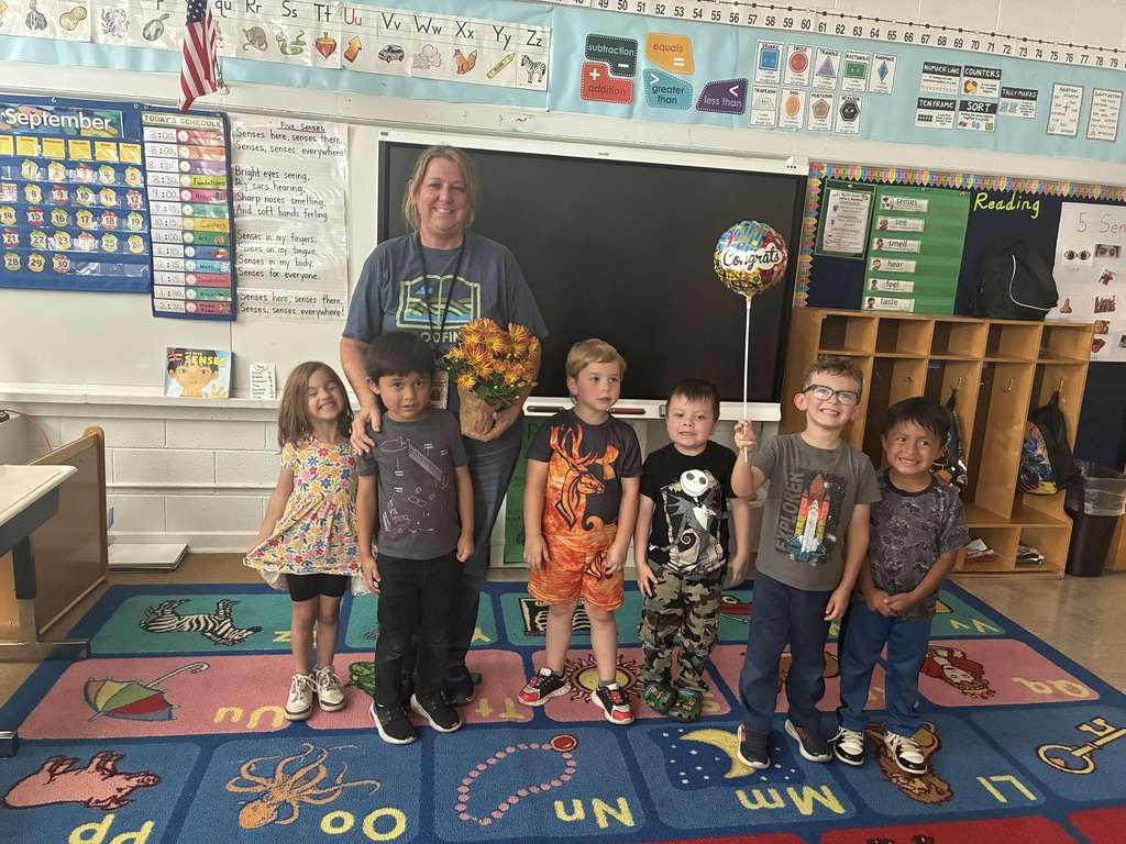 Teacher of the Year, Mrs. Rogers, with students surrounding her. She is holding flowers.