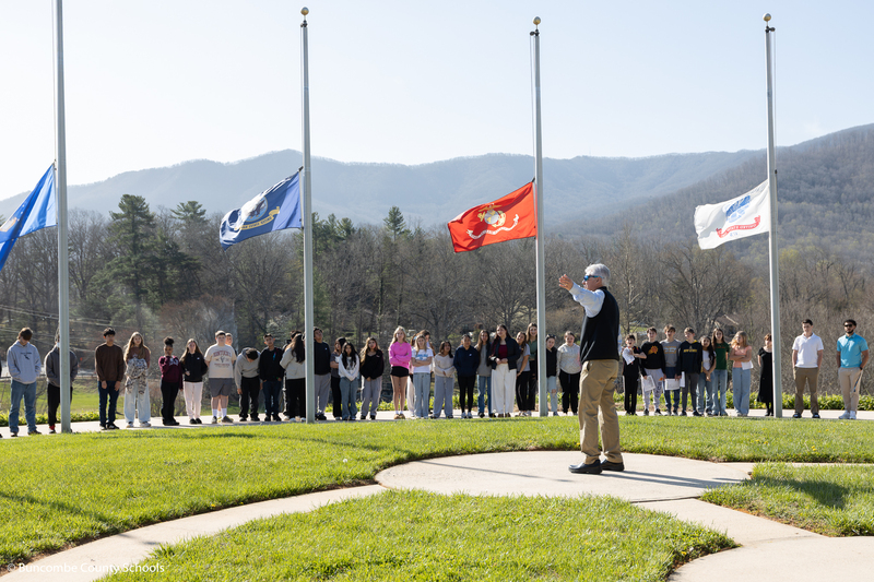 Students gathered around the flag poles at the Veterans Cemetery, listening to the director talk.