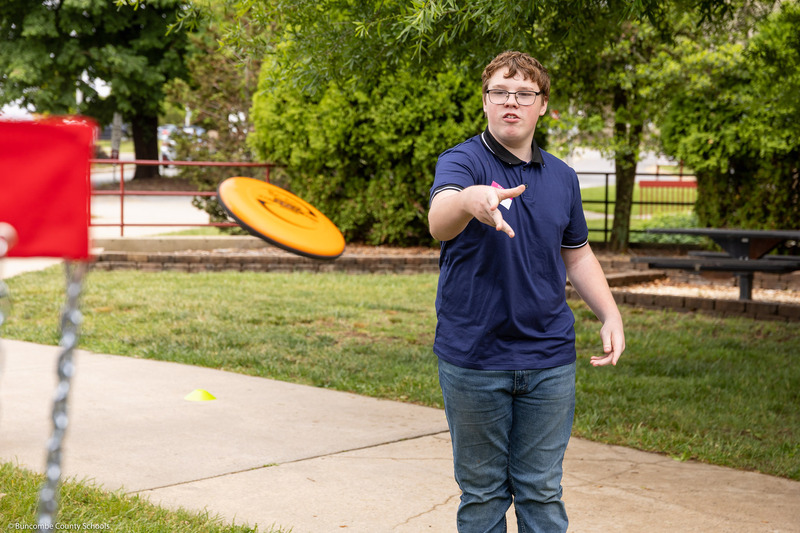 An eighth grader throws a disc at a disc golf pin.