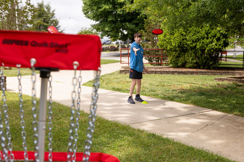 An eighth grader throws a disc at a disc golf pin.