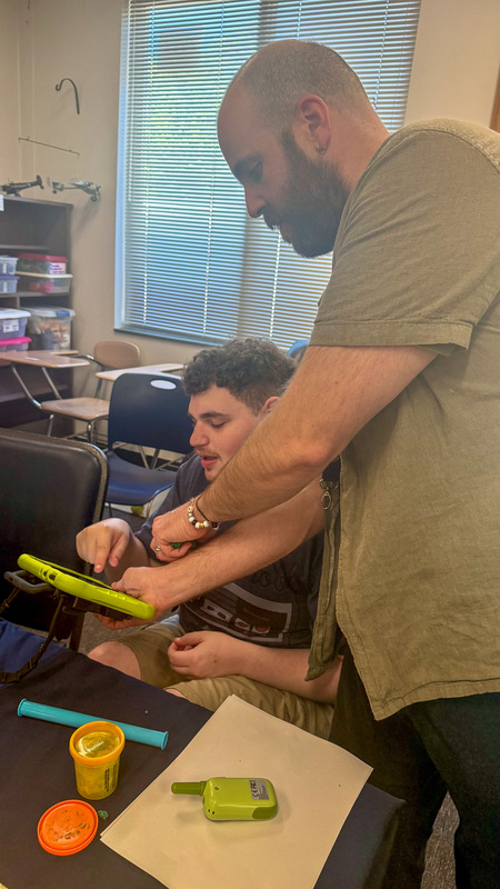 A PEP teacher holds a communication device while a student points.