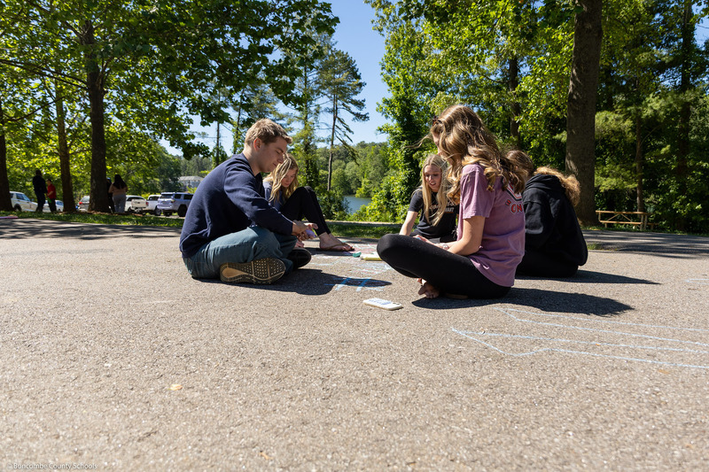 Students sit in a circle and draw with sidewalk chalk.