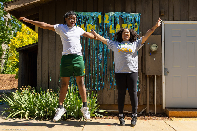 Two students jump in front of a decoration that says "12 Years Later."