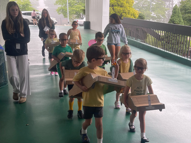 Preschoolers walking into the school wearing cardboard cars.