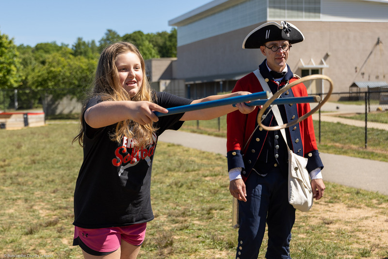 A girl plays an old-timey game involving sticks and a hoop.