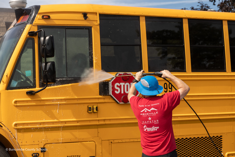 A man uses a pressure washer to spray the school bus stop sign.
