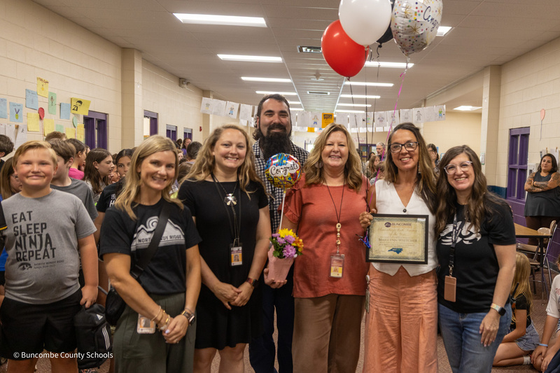 Ms. Whitcher holds her plaque and balloons while standing with principals, math coaches, and students.