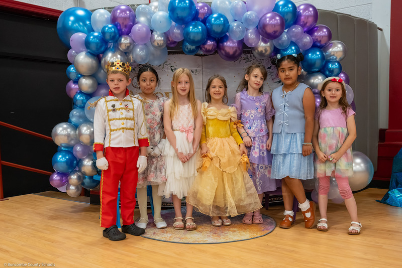 Kids in fairy tale outfits pose in front of a balloon backdrop.