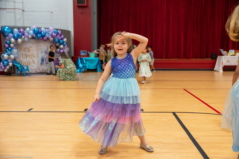 A girl strikes a pose during a dance in the gym.