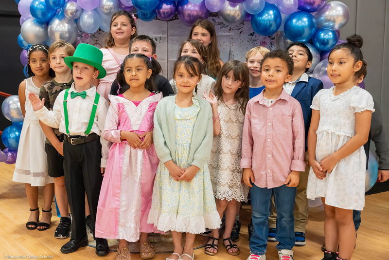 Kids in fairy tale outfits pose in front of a balloon backdrop.