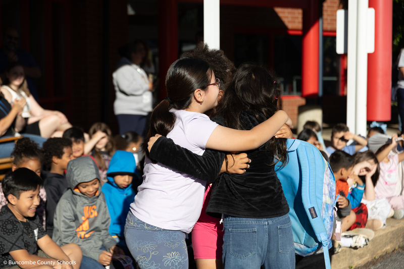 Group of kids hugging their friend as she gets off the firetruck. 