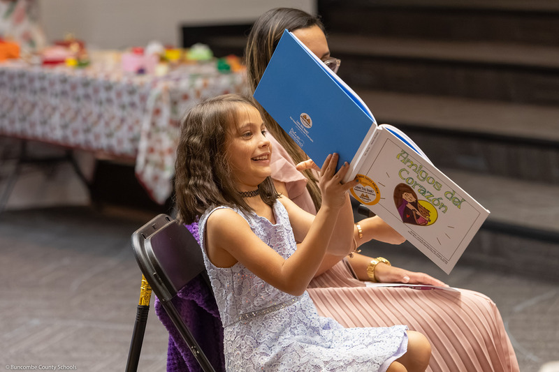A girl shows a book to the class and parents.