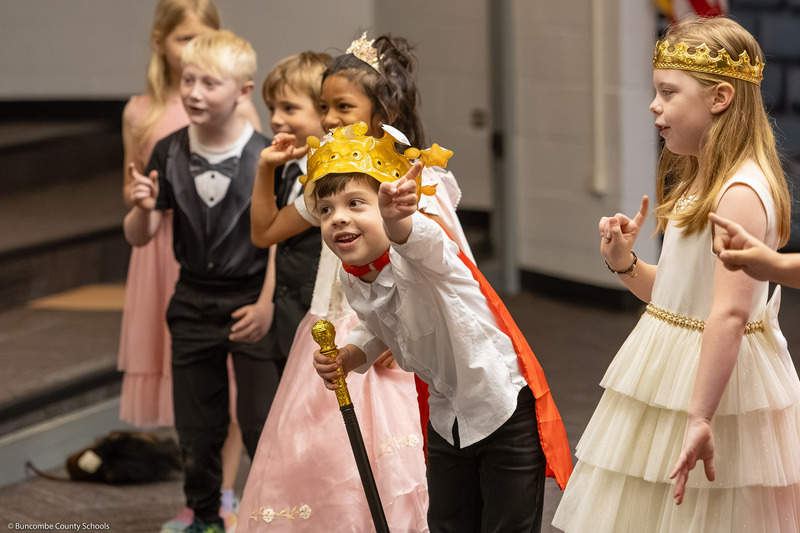 A boy wearing a crown points to the left.