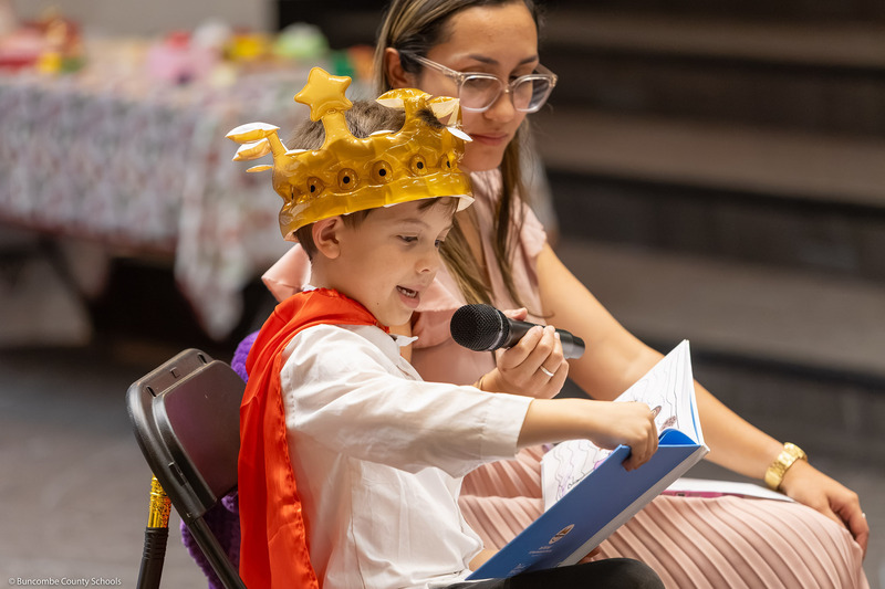 A boy reads a book while wearing a crown.
