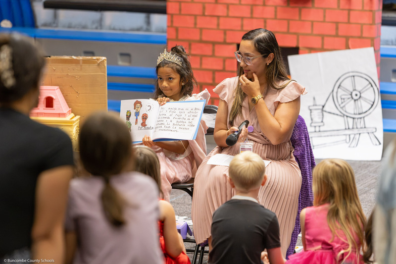 A girl shows a book to the class and parents.