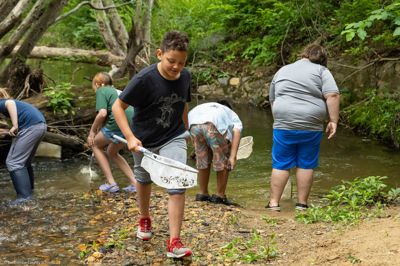 A student walks down the bank while holding a net.