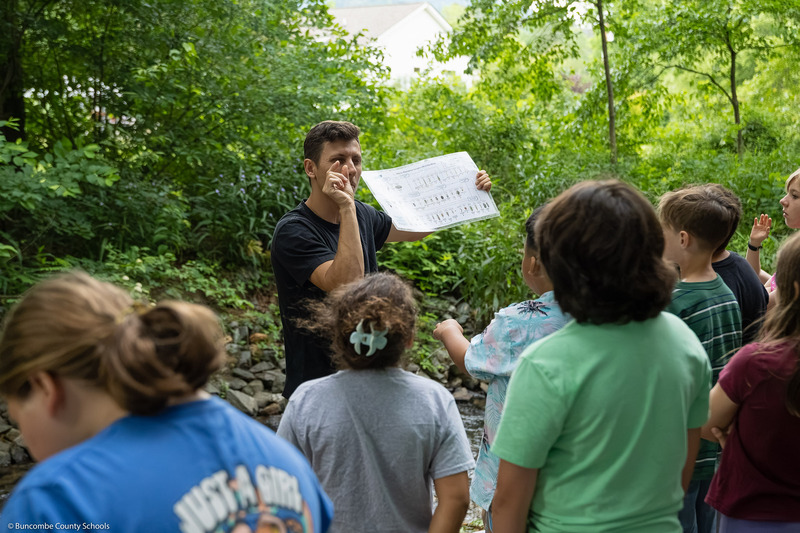 Alex Russell, in-school education coordinator for RiverLink, speaks to students while holding an educational chart.