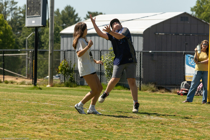 A fielder reaches up to catch a ball while a runner returns to base.