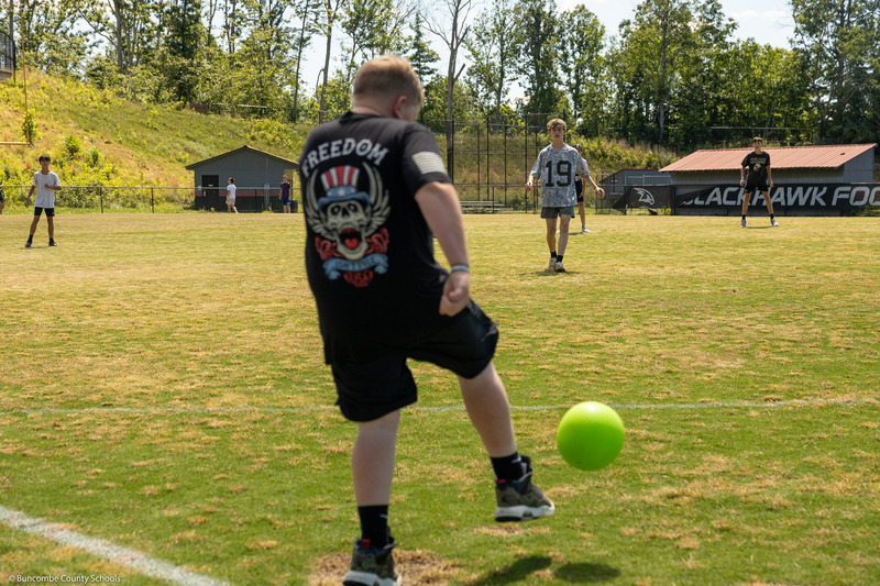 A kicker makes contact with the ball while the pitcher watches.