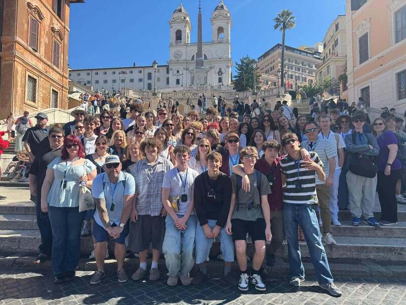 Students pose for a group photo standing in front of classic Roman buildings