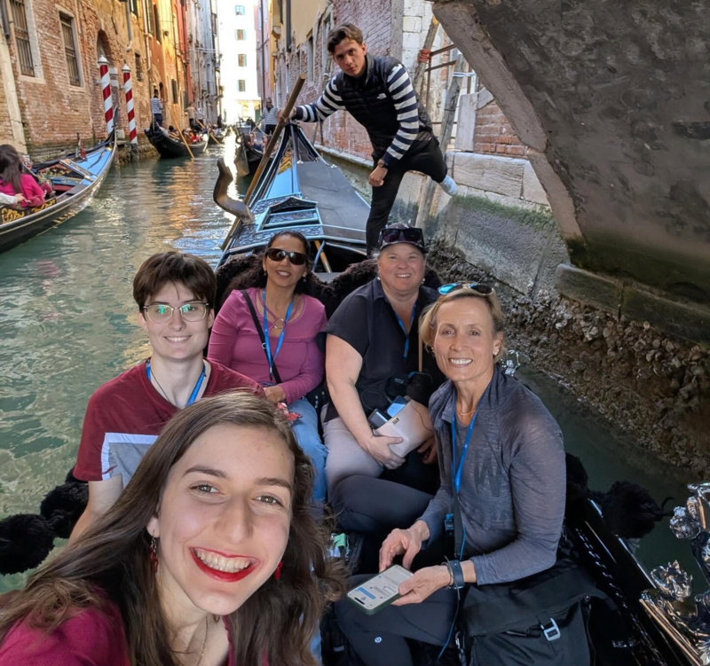 Students smile in a gondola as the boat is paddled by a gondolier